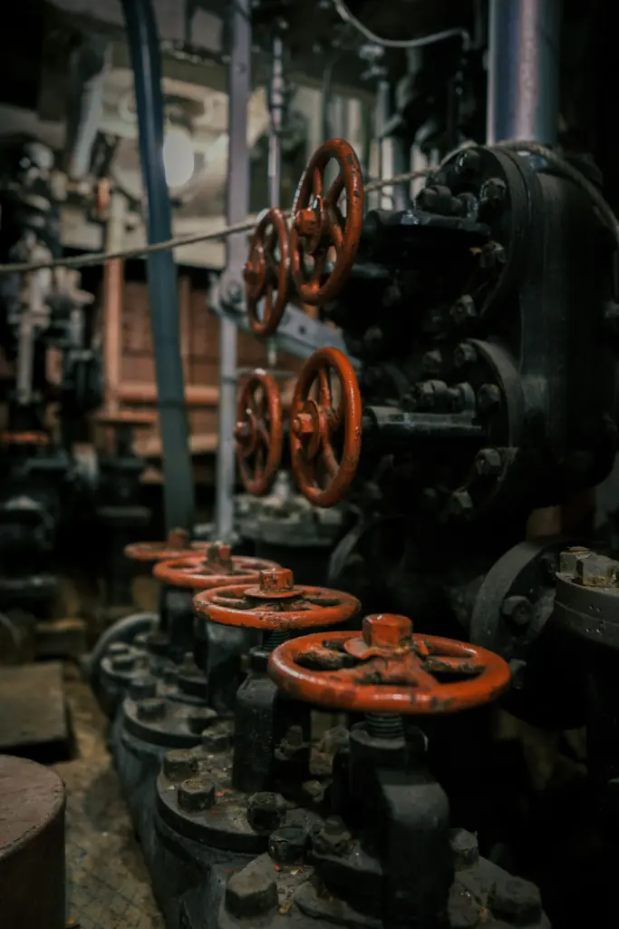 Industrial scene with rusty orange valve wheels attached to dark machinery in a dim, cluttered workshop.
