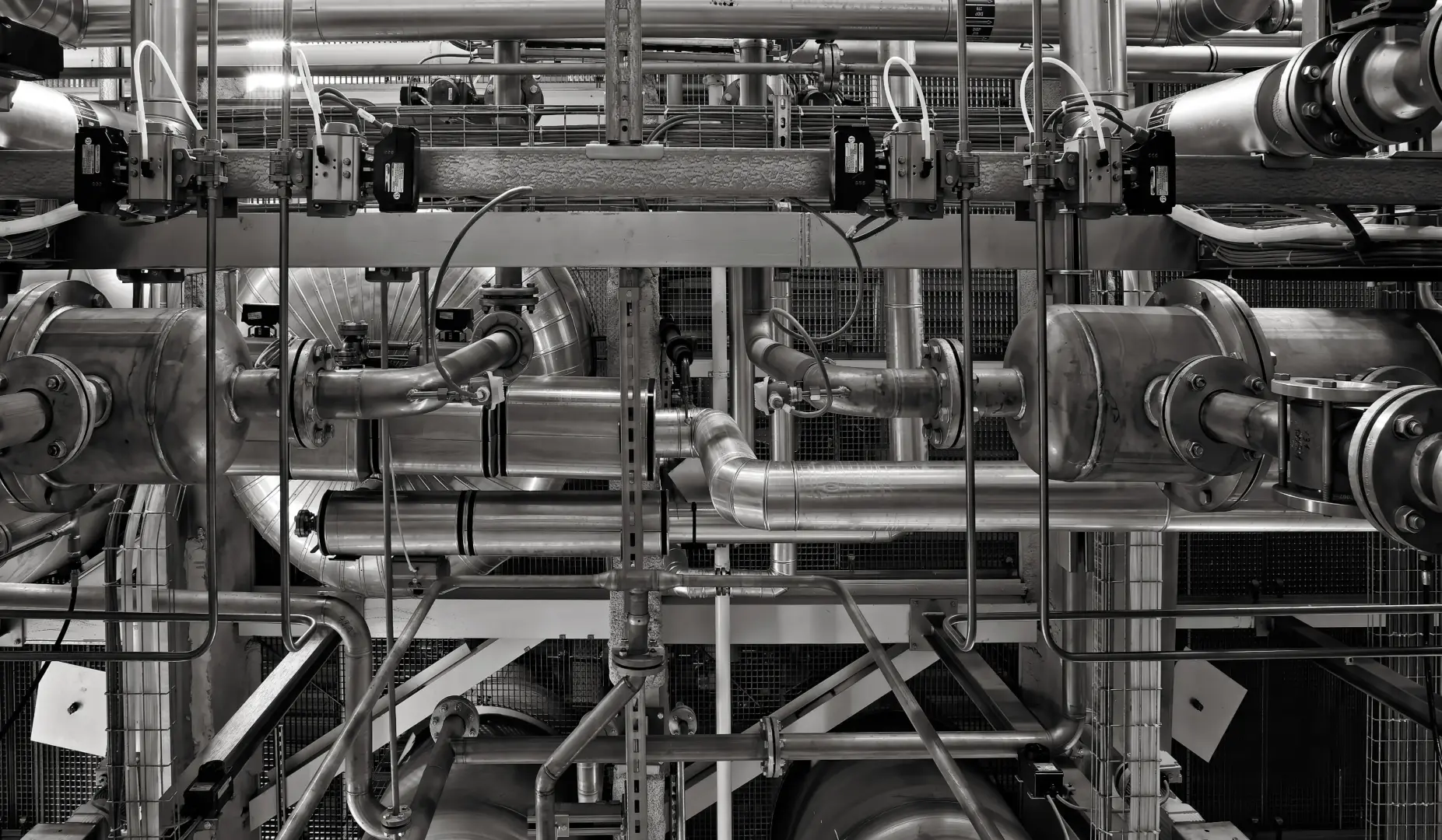 Complex network of stainless steel pipes, valves, and machinery in an industrial plant (black and white).