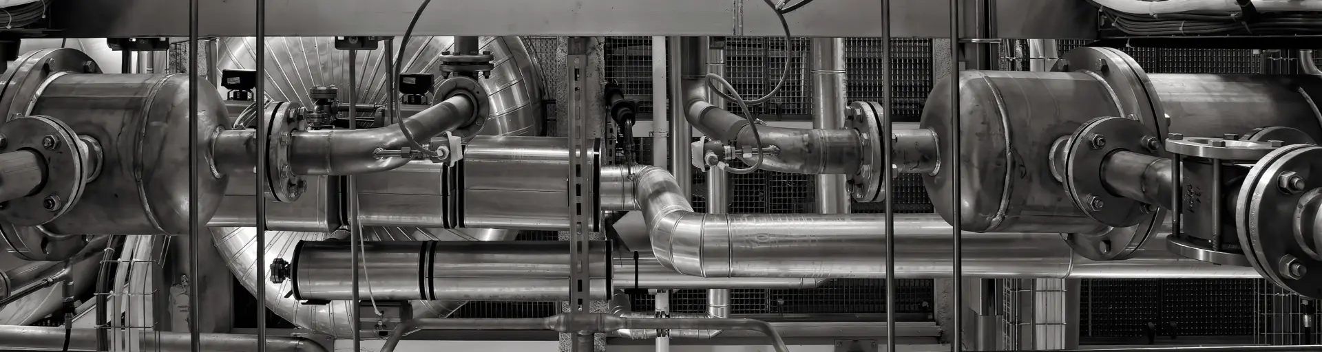 Complex network of stainless steel pipes, valves, and machinery in an industrial plant (black and white).